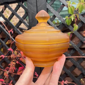 Puede incluir: Una caja de vidrio ámbar vintage con tapa abovedada y diseño geométrico. La caja está hecha de vidrio esmerilado y tiene un aspecto delicado y elegante.