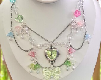 May include: A layered silver chain necklace with a heart-shaped watch pendant. The necklace is adorned with pastel-colored plastic flowers and beads.