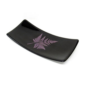 May include: A black glass serving dish with a raised fern design in a light purple color.