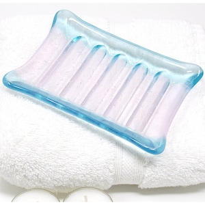May include: A light blue and pink glass soap dish with a ridged design. The dish is made of recycled glass and is perfect for holding soap bars.