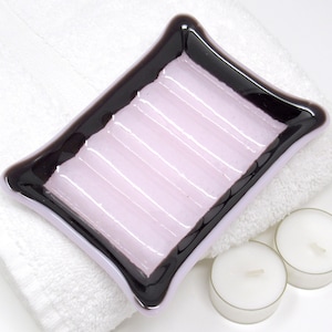 May include: A pink glass soap dish with a black rim. The dish has a ridged surface and is shaped like a rectangle with rounded corners.