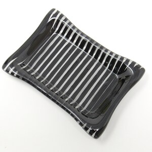 May include: A small, rectangular glass dish with a black and silver striped pattern. The dish has a slightly curved edge and is perfect for holding small items.