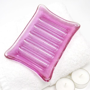 May include: A pink glass soap dish with a ridged surface. The dish is sitting on a white towel.