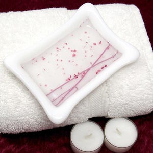 May include: White ceramic soap dish with a pink and white swirl design. The dish is sitting on a white towel.
