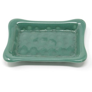 May include: A green ceramic soap dish with a textured surface. The dish has a slightly rounded rectangular shape with rounded edges.