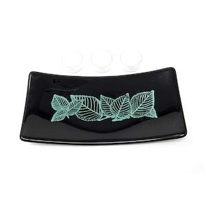 May include: Black glass candle holder with a teal leaf design. Three white tea lights are placed on the holder.