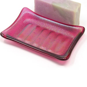 May include: A pink iridescent glass soap dish with a rectangular shape and raised ridges on the bottom.