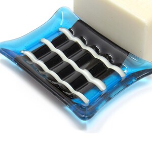 May include: A blue glass soap dish with black and white stripes. The dish is designed to hold a bar of soap.