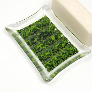 May include: A green and black glass soap dish with a rippled design. The dish is made of clear glass with green and black swirls.
