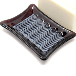May include: A dark purple glass soap dish with a wavy white design. The dish is empty and has a slightly curved shape.