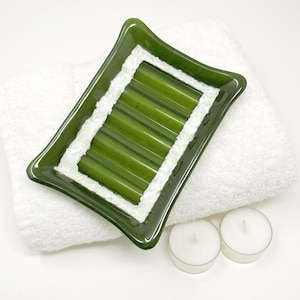 May include: A green glass soap dish with a white border and five ridges. The dish is sitting on a white towel.