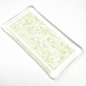 May include: A rectangular glass dish with a clear border and a central section filled with small, light green, irregular shapes. The dish is set against a white background, showcasing its translucent qualities.