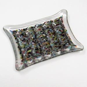 May include: A clear glass soap dish with a rectangular shape and curved edges. The dish features a colorful mosaic design of small, irregular pieces in various colors. The soap dish is designed to hold a bar of soap.