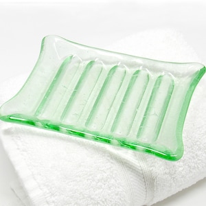 May include: A light green glass soap dish with raised ridges on the bottom. The dish is sitting on a white towel.