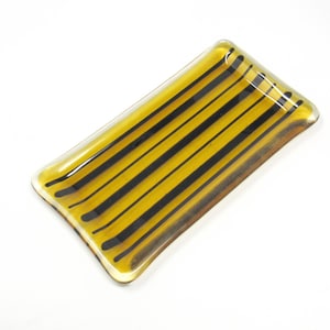 May include: A small, rectangular glass dish with a yellow amber color and black stripes.