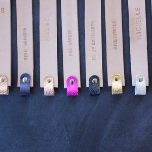 May include: Eight leather bookmarks with different text and colored tassels. The bookmarks are beige with gold lettering. The tassels are turquoise, brown, beige, pink, black, gold, silver, and gray.