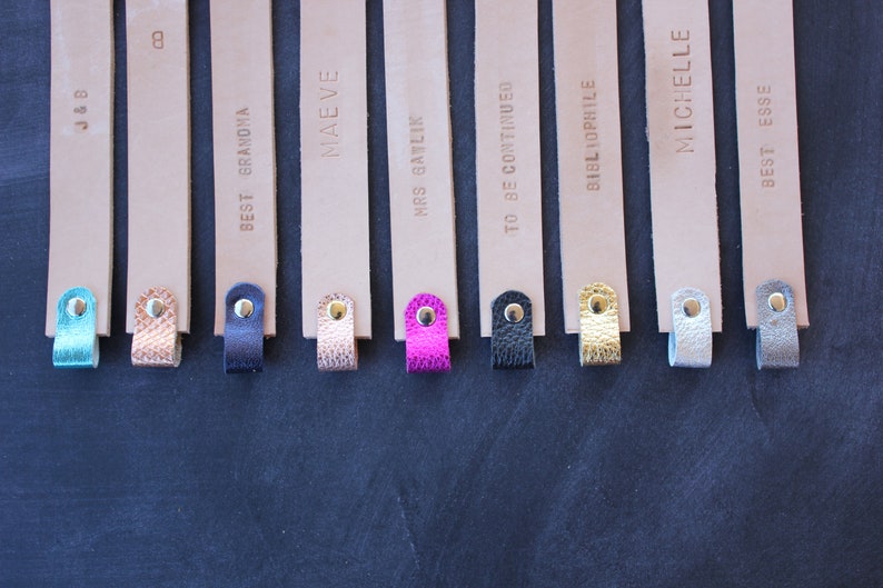 May include: Eight leather bookmarks with different text and colored tassels. The bookmarks are beige with gold lettering. The tassels are turquoise, brown, beige, pink, black, gold, silver, and gray.