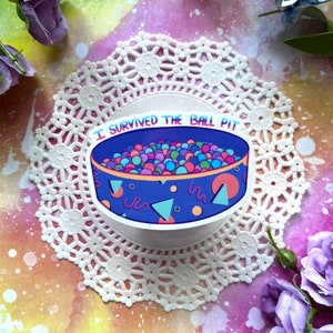 May include: A sticker with a blue and purple ball pit with colorful balls and the text "I survived the ball pit".