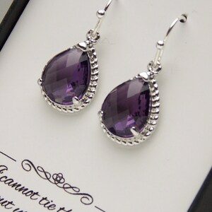 May include: A pair of silver dangle earrings with a teardrop-shaped purple gemstone. The earrings have a rope-like design around the gemstone.