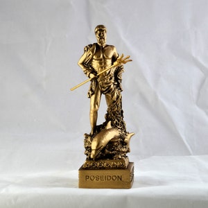 May include: A gold-colored statue of Poseidon, the Greek god of the sea, holding a trident. The statue depicts Poseidon standing on a base with a dolphin. The word "POSEIDON" is inscribed on the base.