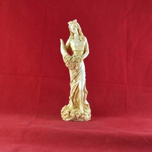 Op de afbeelding: Een gouden beeld van een vrouw die een hoorn des overvloeds vol bloemen vasthoudt. Het beeld staat op een voetstuk met een bloemenmotief.