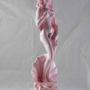 May include: A pink ceramic statue of a woman standing on a seashell. The statue is a reproduction of the famous Venus de Milo sculpture.