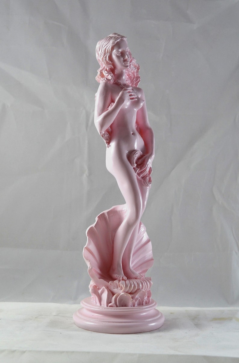 May include: A pink ceramic statue of a woman standing on a seashell. The statue is a reproduction of the famous Venus de Milo sculpture.