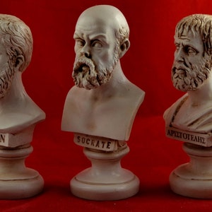 May include: Three white plaster busts of famous Greek philosophers: Plato, Socrates, and Aristotle. Each bust is on a white pedestal with the philosopher's name inscribed on the front.