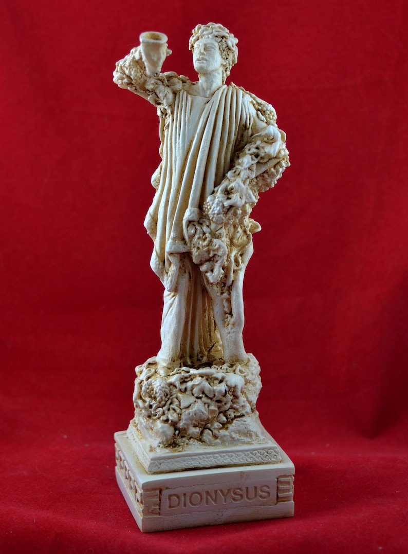 Op de afbeelding: Cr&egrave;mekleurig beeld van Dionysus, de Griekse god van de wijn, op een rode achtergrond. Het beeld houdt een beker vast en is versierd met wijnranken. De basis van het beeld is gegraveerd met de naam "DIONYSUS".