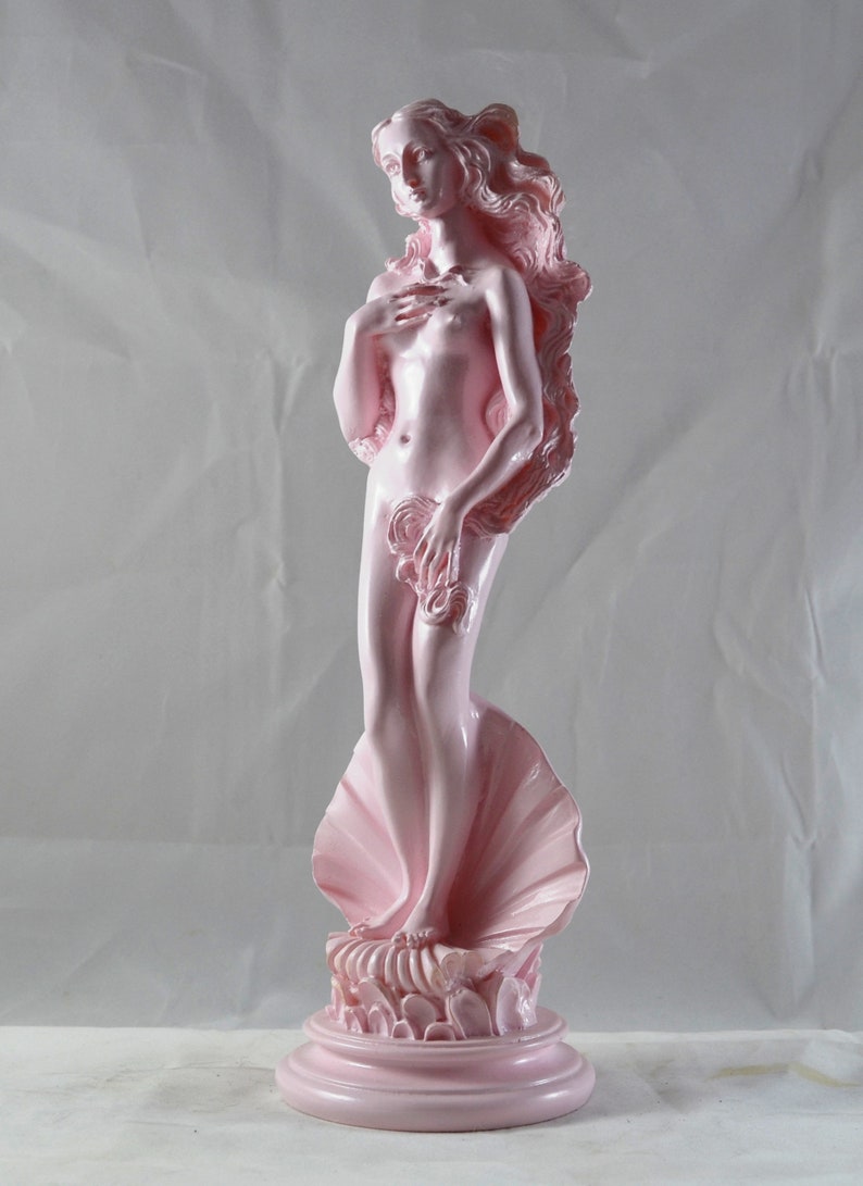 May include: A pink ceramic statue of the Birth of Venus, a classical sculpture of a woman standing on a seashell. The statue is on a pink base.