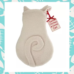 Puede incluir: Un calcetín navideño con forma de gato, de color crema. Presenta una cola enroscada y orejas. Una etiqueta roja con el texto "Santa I've been a Good Cat" está sujeta con una cinta roja. Fondo blanco, borde turquesa.