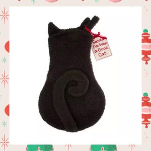 Op de afbeelding: Zwarte katvormige kerstsok met een gekrulde staart en kleine oren. Een label bevestigd met een rood lint leest "Santa I've been a Good Cat". De sok is gemaakt van een zacht, getextureerd materiaal.