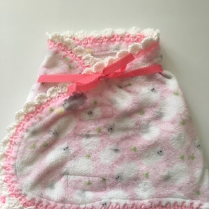 May include: A pink and white baby blanket with a crocheted border and a pink ribbon tied in a bow. The blanket has a small animal print.