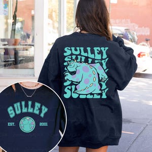May include: Navy blue sweatshirt featuring a Sulley graphic from the movie Monsters, Inc. The design includes the word "SULLEY" in a teal font, along with an image of Sulley. The sweatshirt also has the text "EST. 2001".