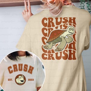 May include: Beige t-shirt featuring a cartoon turtle character with the text "CRUSH" in brown. The back of the shirt has a larger graphic of the turtle and the words "CRUSH IS CRUSH". The shirt also has the text "EST. 2003".