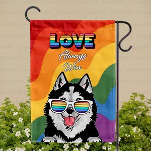 May include: A garden flag featuring a smiling husky wearing rainbow-colored sunglasses. The flag has a rainbow background and the words "LOVE Always Win" in colorful text. The flag is displayed on a black metal stand.