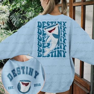 May include: Light blue sweatshirt with a whale shark graphic and the text "DESTINY" repeated in a retro style on the back. The front of the sweatshirt has the text "DESTINY EST. 2016" with a whale shark graphic.