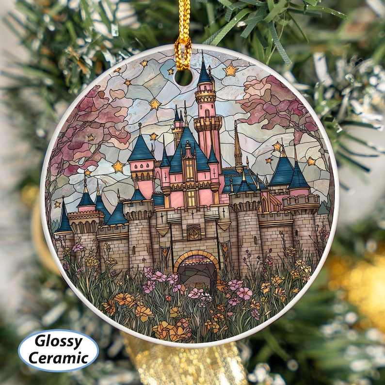 May include: A round, glossy ceramic ornament featuring a colorful stained-glass design of a fairytale castle with pink, blue, and gray tones. The castle is surrounded by flowers and stars, with a gold hanging cord.