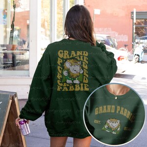 May include: Green sweatshirt with a graphic print of a character from the movie "Labyrinth" with the text "Grand Pabbie" on the back. The front of the sweatshirt has the text "Grand Pabbie Est. 80's" with a smaller graphic of the character.