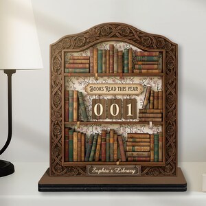 May include: A wooden bookshelf-shaped decorative piece with the text "Books Read This Year" and "001". The bookshelf is filled with miniature books in various colors. The bottom of the piece reads "Sophia's Library".