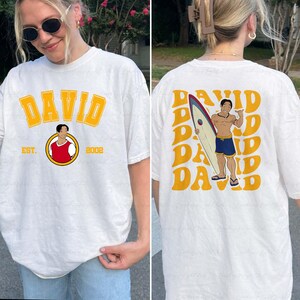 a woman wearing a t - shirt with a picture of a man holding a surf