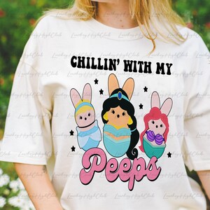 May include: Cream-colored t-shirt with the text "CHILLIN' WITH MY Peeps." The graphic features three cartoon characters in Easter egg shapes with bunny ears. The characters are in blue, teal, and pink, with black stars.
