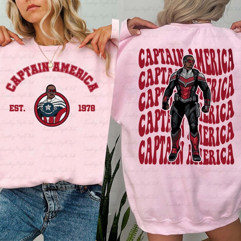 May include: A light pink sweatshirt featuring the words "CAPTAIN AMERICA" in red arched text. Below the text is a circular graphic with a portrait of a character. The back of the sweatshirt has a repeating pattern of the words "CAPTAIN AMERICA" and a full body image of the character.