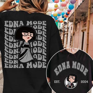 May include: Black t-shirt featuring a cartoon illustration of Edna Mode from The Incredibles. The design includes the text "EDNA MODE" in a repeating pattern on the back and a smaller circular design with the text "EDNA MODE" and "EST. 2004" on the front.