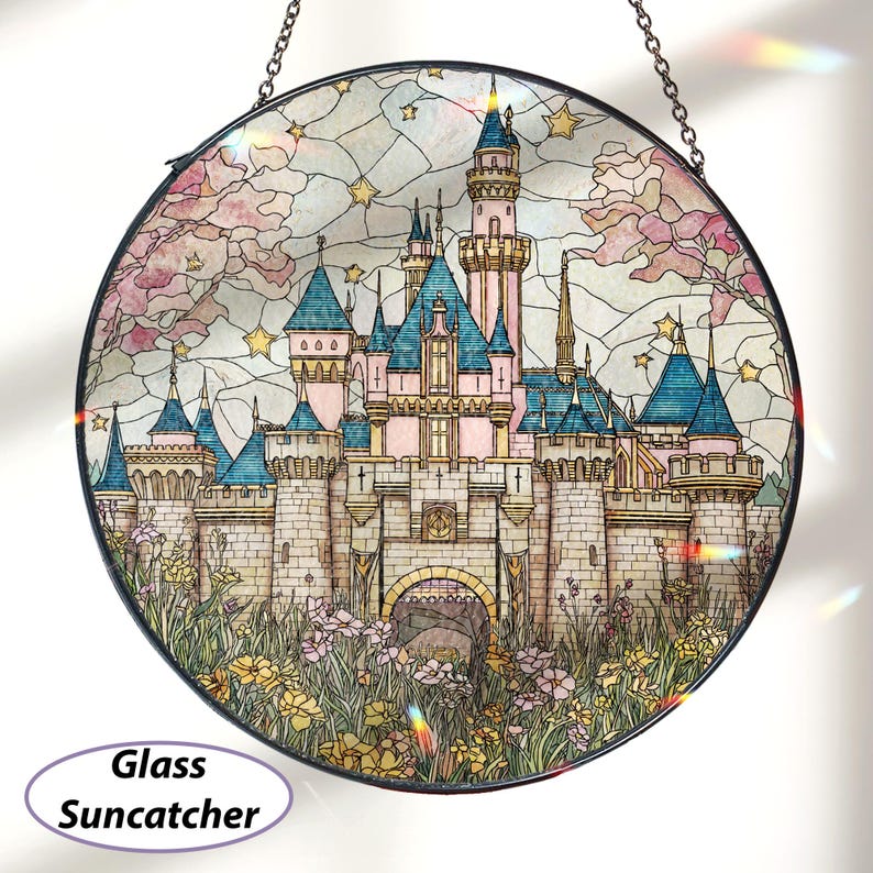 May include: Round glass suncatcher featuring a fairytale castle with pink, blue, and beige tones. The castle has multiple turrets and is surrounded by flowers and foliage. The suncatcher is suspended by a chain and has the words "Glass Suncatcher" on it.