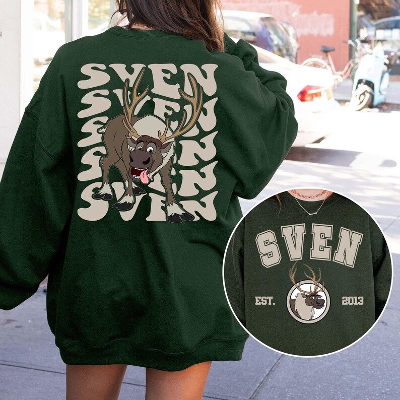 Pode incluir: Camisola verde escuro com o nome "SVEN" num design ondulado empilhado e um gr&aacute;fico de rena de desenho animado. A rena tem grandes chifres e est&aacute; a mostrar a l&iacute;ngua. Uma imagem menor do design est&aacute; no canto inferior direito.