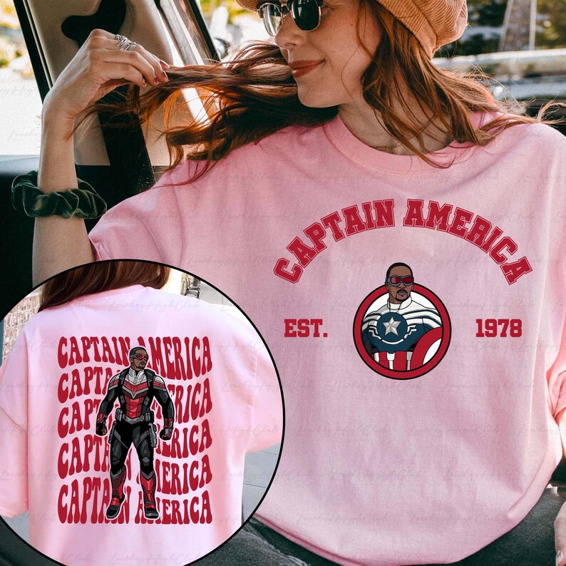 May include: Pink t-shirt featuring a Captain America graphic. The front design includes the words "CAPTAIN AMERICA" in red, with an image of Captain America in a shield, and the text "EST. 1978". The back of the shirt has a Captain America graphic and the words "CAPTAIN AMERICA" repeated.
