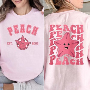May include: Light pink sweatshirt with the word "PEACH" in a pink, block letter font. Below the word "PEACH" is a pink starfish with a smiling face. The back of the sweatshirt has the word "PEACH" repeated with a pink starfish.