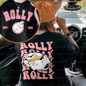 May include: Black t-shirt with a pink "ROLLY" graphic and a cartoon Dalmatian dog holding a corn cob. The text "EST. 1961" is also on the shirt.