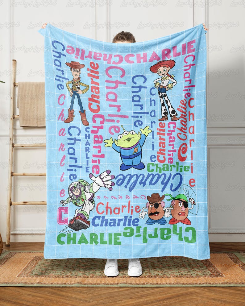 May include: A light blue fleece blanket featuring a white grid pattern and the name Charlie repeated in various colors and fonts. The design includes printed illustrations of Woody, Jessie, an alien, Buzz Lightyear, and Mr. Potato Head characters.
